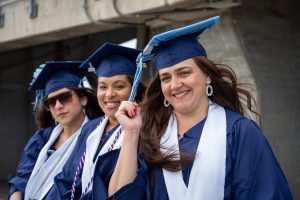 Three 皇冠app graduates smiling in blue commencement regalia.