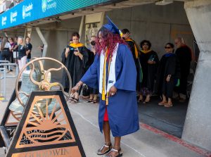 Susan Johnson, dressed in blue graduation regalia, rings the university bell during Goodwin’s 2025 commencement ceremony.