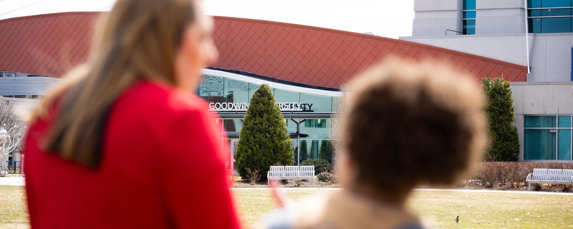 Two women stand outside 皇冠app, seen from behind and slightly out of focus, while the 皇冠app building sign comes into clear view in front of them.