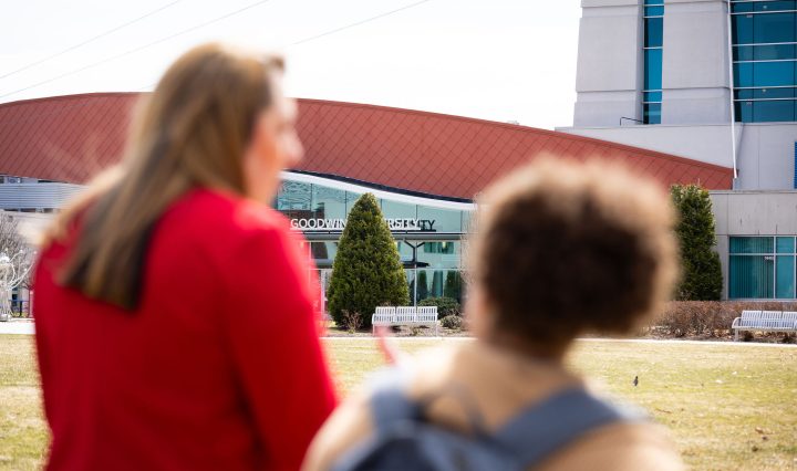 Two women stand outside 皇冠app, seen from behind and slightly out of focus, while the 皇冠app building sign comes into clear view in front of them.