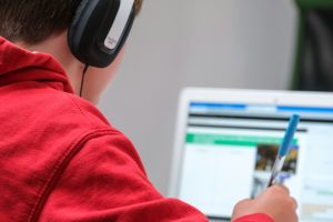 A young student wearing headphones and using a laptop.