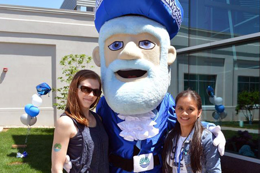 Two students posing with the Navigator mascot